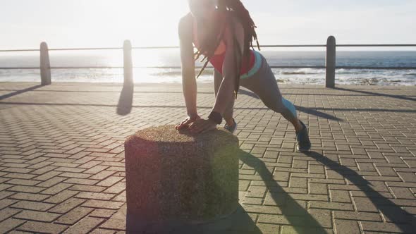 African american woman in sportswear doing press ups on promenade by the sea