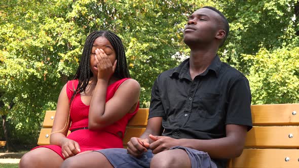 A Black Man and a Black Woman Sit on a Bench in a Park and Act Frustrated