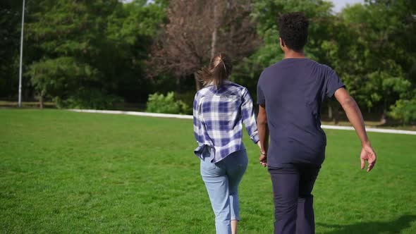 Back View Follow Shot of Cute Attractive International Couple Holding Hands and Running on the Field