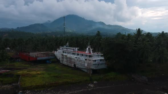 Aerial drone view of an abandoned cruise shipwreck on an isolated tropical island with a dormant vol