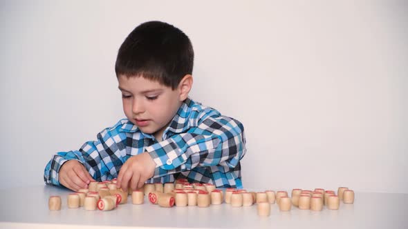 A Preschool Boy Plays Lotto Folds Barrels with Numbers on the Table