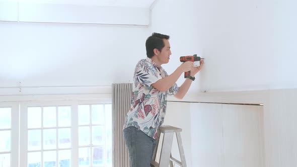 Asian Man On A Ladder Use Electric Drill And Install Cctv Camera On Wall For Security