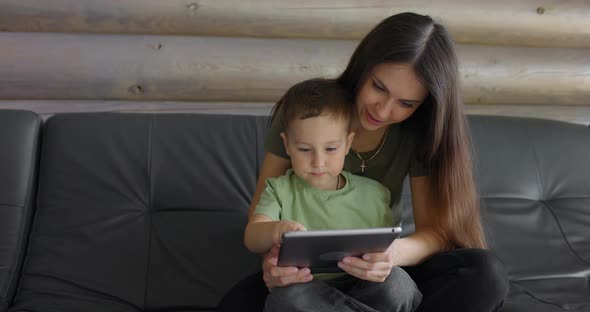 Young Smiling Mother Explaining to Her Young Son How to Properly Complete a Task in an Online Game