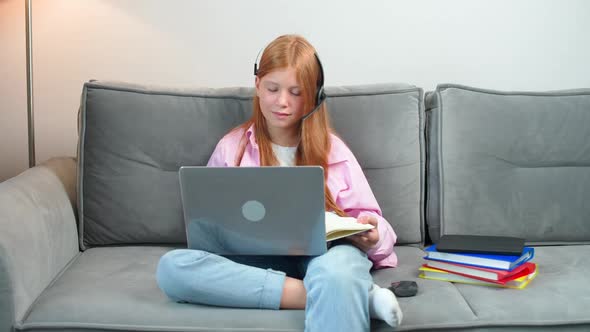 Distance Learning Redhaired Teen Girl Sitting on the Couch in Living Room and Uses a Laptop to Study