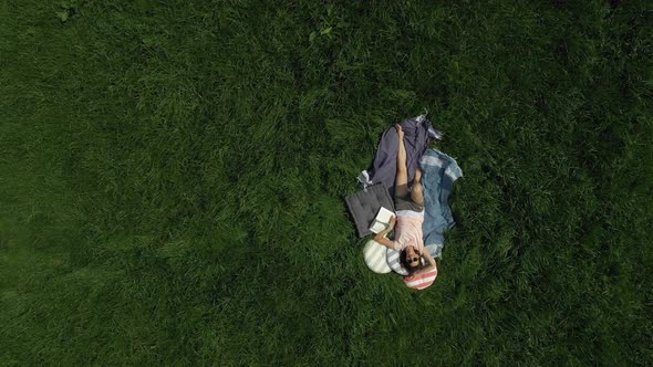 Push-out drone shot of a woman realxing on a meadow