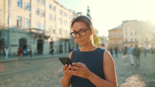 Woman Walking Down an Old Street and Using Smartphone at Sunset. Slow Motion