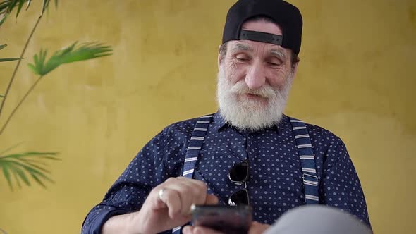 70-aged Bearded Man in Stylish Cap which Sitting Near Yellow Wall 