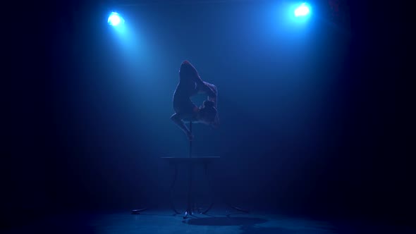 Acrobat Girl on Stage Does Acrobatic Stunts Standing on Her Hands . Smoke Blue Background