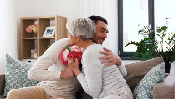 Adult Son Giving Flowers To Senior Mother at Home