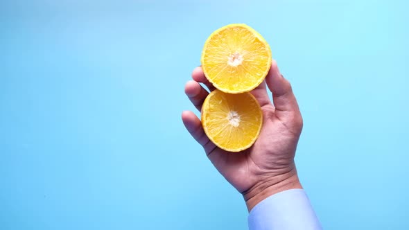 Man Hand Holding Slice of Orange Fruit i Against Blue Background