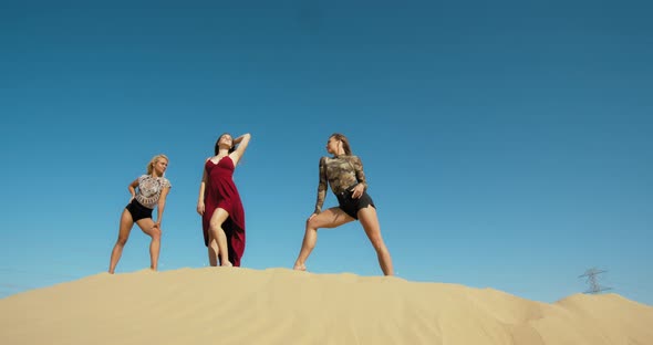 Three Beautiful Young Women are Posing on Top of a Sand Dune