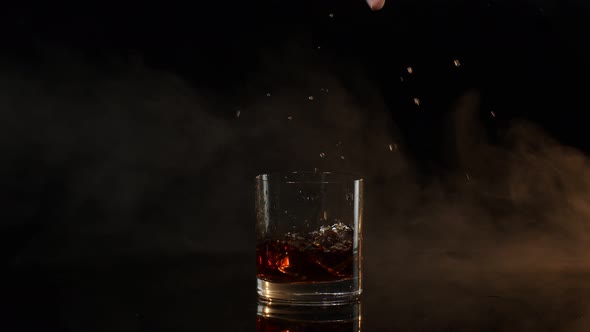 Barman Dropping Ice Cubes Into Drinking Glass with Golden Whiskey Cognac Brandy on Black Background
