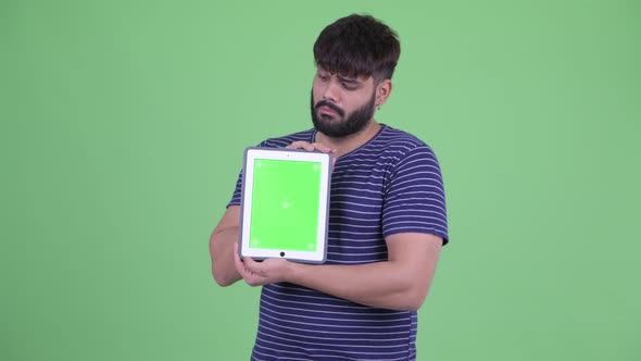 Happy Young Overweight Bearded Indian Man Thinking While Showing Digital Tablet