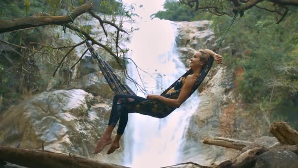 Girl Lies on Hammock Against Pictorial Waterfall