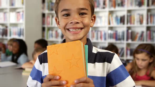 Portrait of schoolboy holding books in library