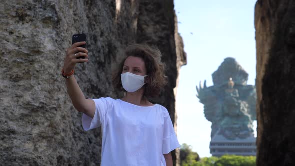 Caucasian Girl in Protective Face Mask Taking Selfie in Front of a Temple in Bali
