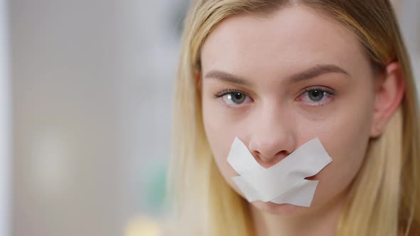 Headshot of Young Caucasian Woman Taking Off Tape From Mouth Looking at Camera with Serious Facial