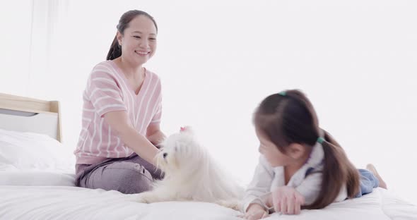 Mother and daughter playing with white dog on bed 4