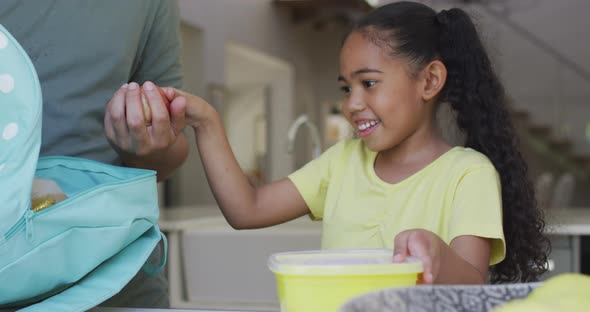 Happy biracial father and daughter packing lunch for school