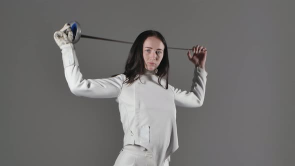 Portrait of a Young Woman in a Protective White Fencing Suit Holding a Sword Confidently Looking at