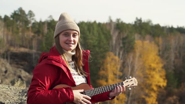 Woman Sits on Rock on and Holds the Ukulele