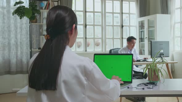 Asian Woman Doctor Is Using Laptop Computer With Mock Up Green Screen Display In Workplace