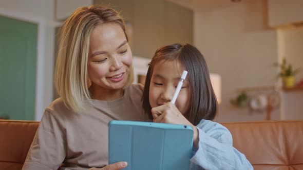 Asian Family and Little Daughter Sit Together on Sofa at Home With Tablet Device Choose Buy Goods on