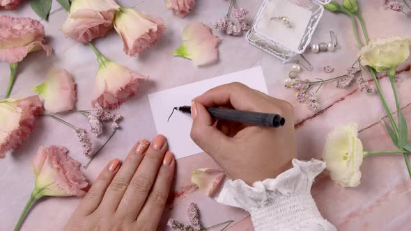 Hands writing SMILE on a card near pink flowers close up on a marble table