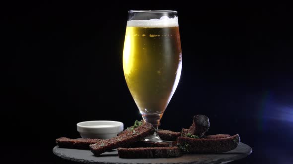 Light Chilled Cold Beer in Glass and Pieces of Dark Bread Croutons on Black Wooden Background, Food