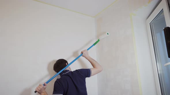 Caucasian Man Paints a Wall with a Roller Over His Head with His Hands