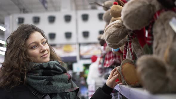 Young Curlyhaired Woman Chooses Christmas Presents in Mall