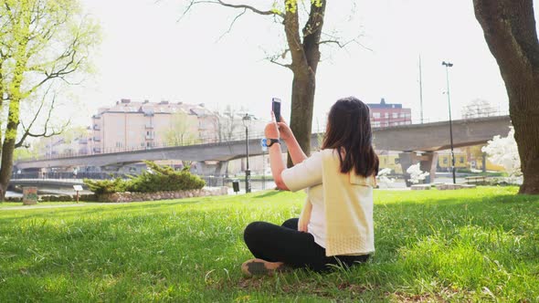 Back view of Asian Straight hair woman sitting on the ground and taking a photo of river