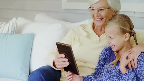 Happy grandmother and little girl seating on sofa and using tablet 4K 4k