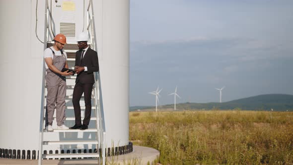 Multiracial Partners Standing on Stairs Near Wind Turbine and Looking on Screen