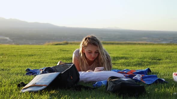 Shot of a beautiful young woman laying on a blanket on the grass at a park. The girl is staring at h