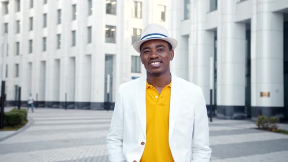 Black successful businessman in yellow t shirt and white suit jacket walks along