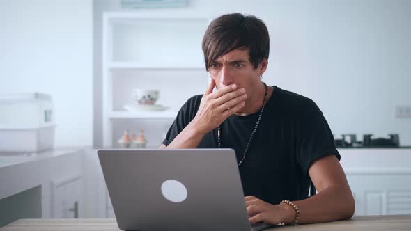 Shocked Male Watching Bad News on a Laptop and Covering His Mouth in Horror While Sitting at the