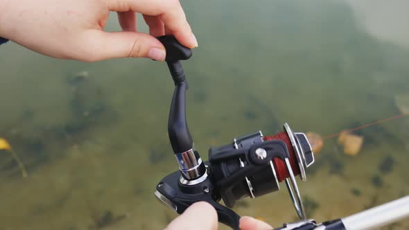 Close-up of a Fisherman Woman with a Handle Rotates a Three-axis Spinning Reel. Fishing in the Pond