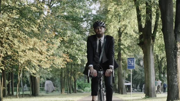 Businessman Riding a Bike in City Park Wearing Suit and Helmet Front View