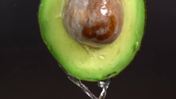 Water falling from avocado on black background. Avocado slice and water splashing, drops of juice