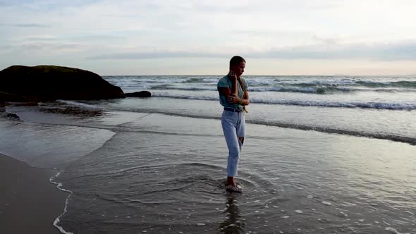 Slow motion: beautiful blond woman walking on shoreline under sunset touching long hair.