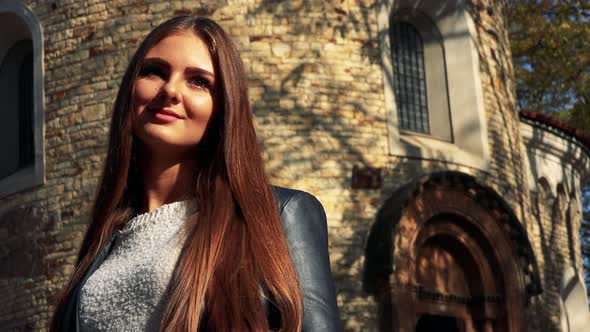 Young Beautiful Woman Smiles To Camera with Old Building in the Background - Closeup