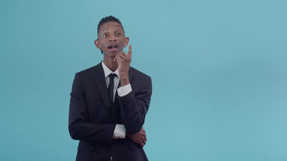 Black man with dreadlocks in a suit thinks, propped up chin with hand and finding the idea smiling l