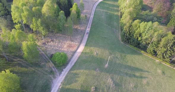 Aerial drone view of a country dirt road with green trees and hills.