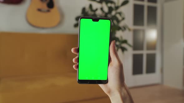 Handheld Camera Point of View of Woman at Modern Room Using Phone With Green Mockup Screen