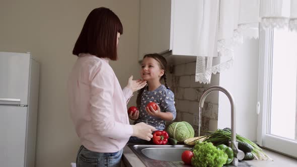 A Young Beautiful Mother and Her Cute Little Daughter Wash Vegetables Under the Tap with Water