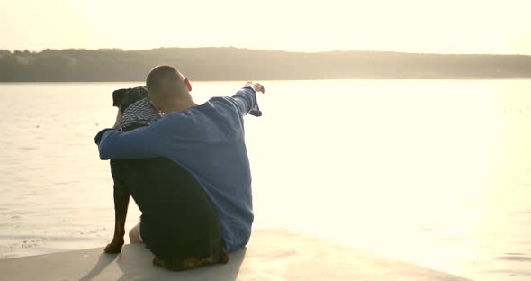 Man and Dog Sitting on the Dock at a Lake