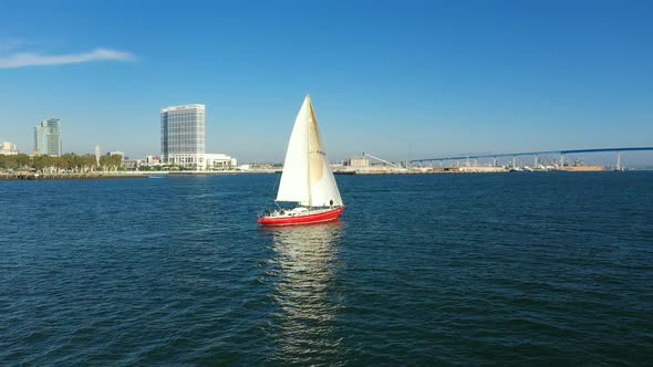 Red sailboat on the San Diego Bay with a view of San Diego's skyline