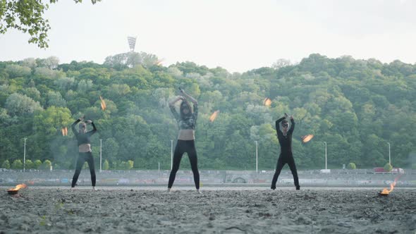 Young Slim Man and Two Beautiful Women Simultaneously Perform Show with Flame