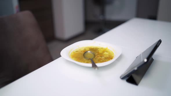 Healthy kid eating at home. Little boy watching tablet while eating on kitchen